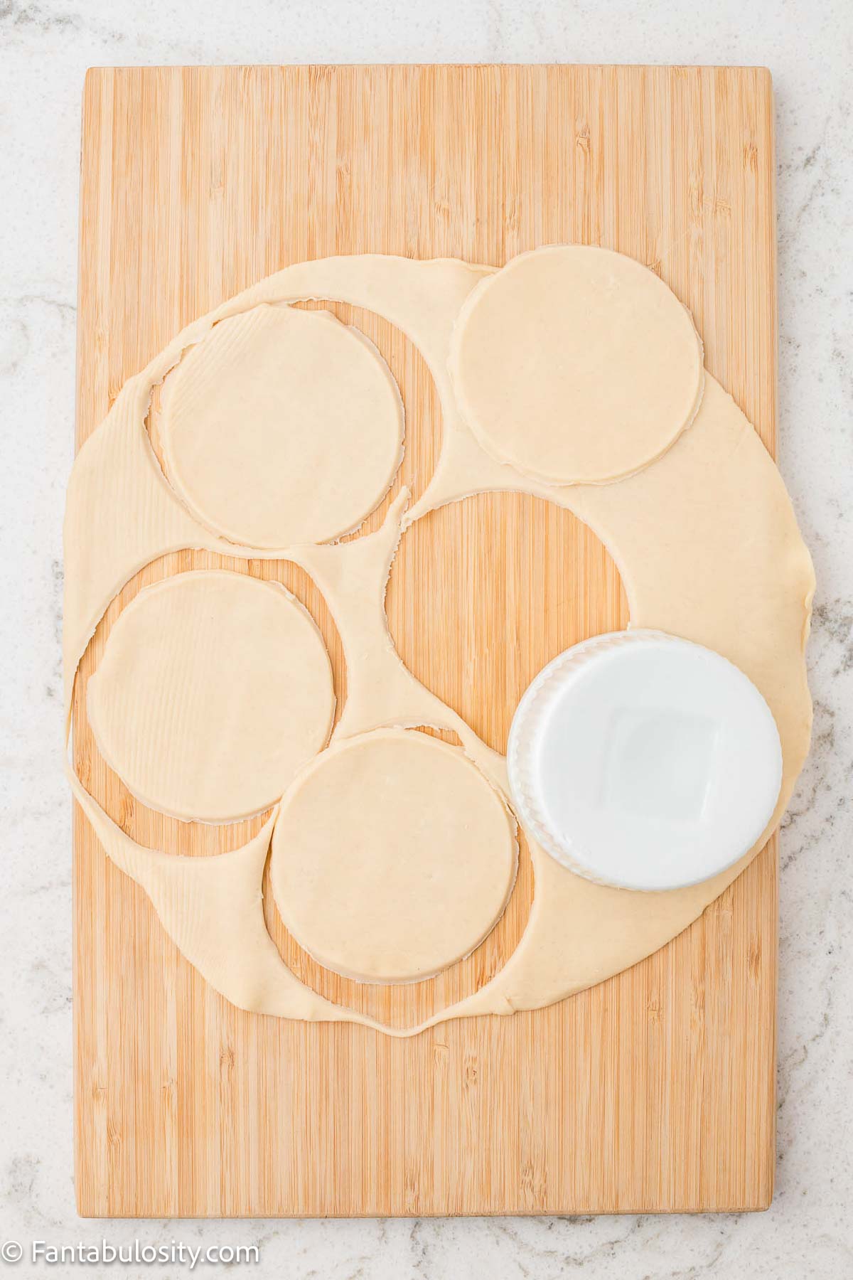 Pie crust with circles cut out, sitting on a wooden cutting board.