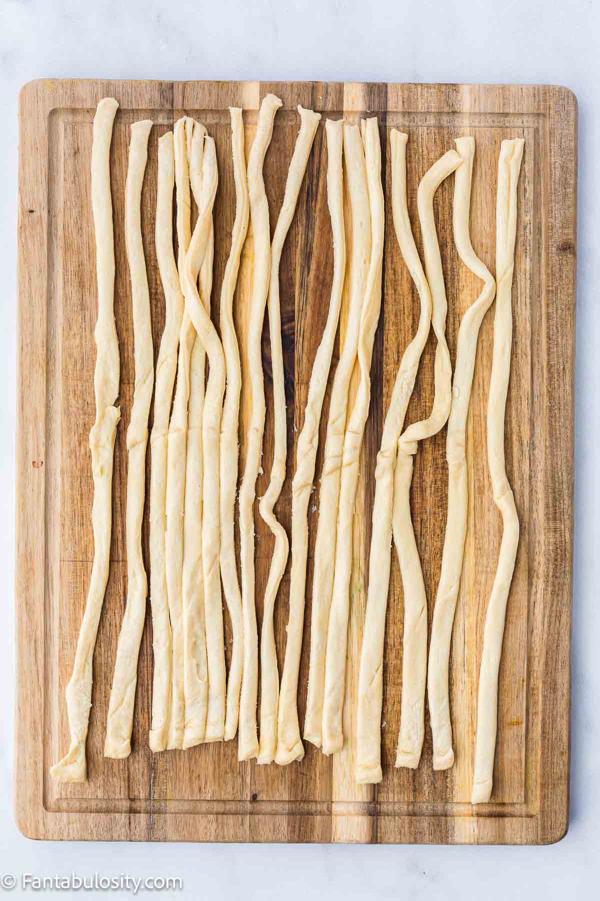 Crescent rolls cut in to thin strips, sitting on wooden cutting board.