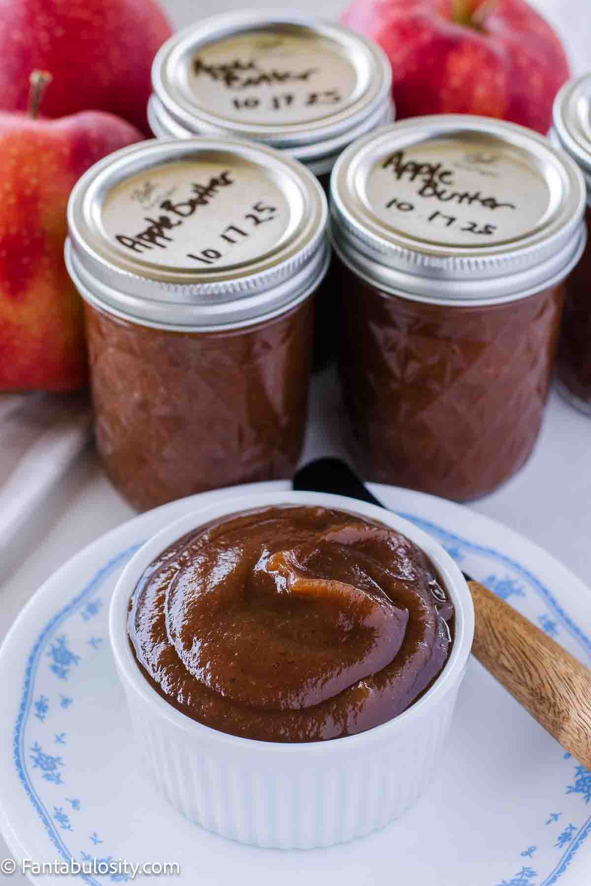 Small bowl full of slow cooker apple butter, next to canned apple butter.