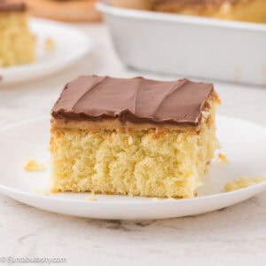 A slice of tandy cake on a round plate, sitting next to the rest of the cake.