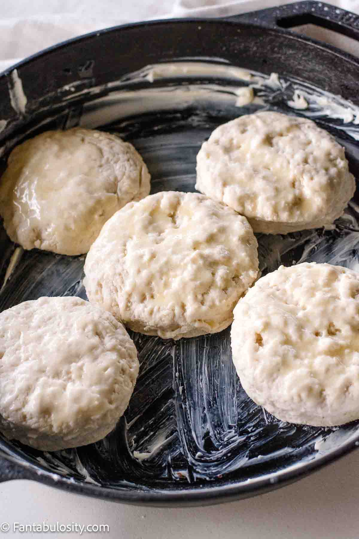 Unbaked biscuits in cast iron skillet, with melted butter brushed on top.