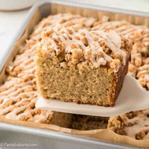 A slice of applesauce crumb cake on spatula, being held above pan.