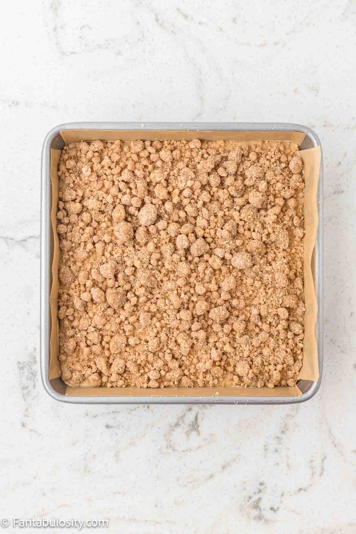 Unbaked applesauce crumb cake with crumb topping in square baking dish.