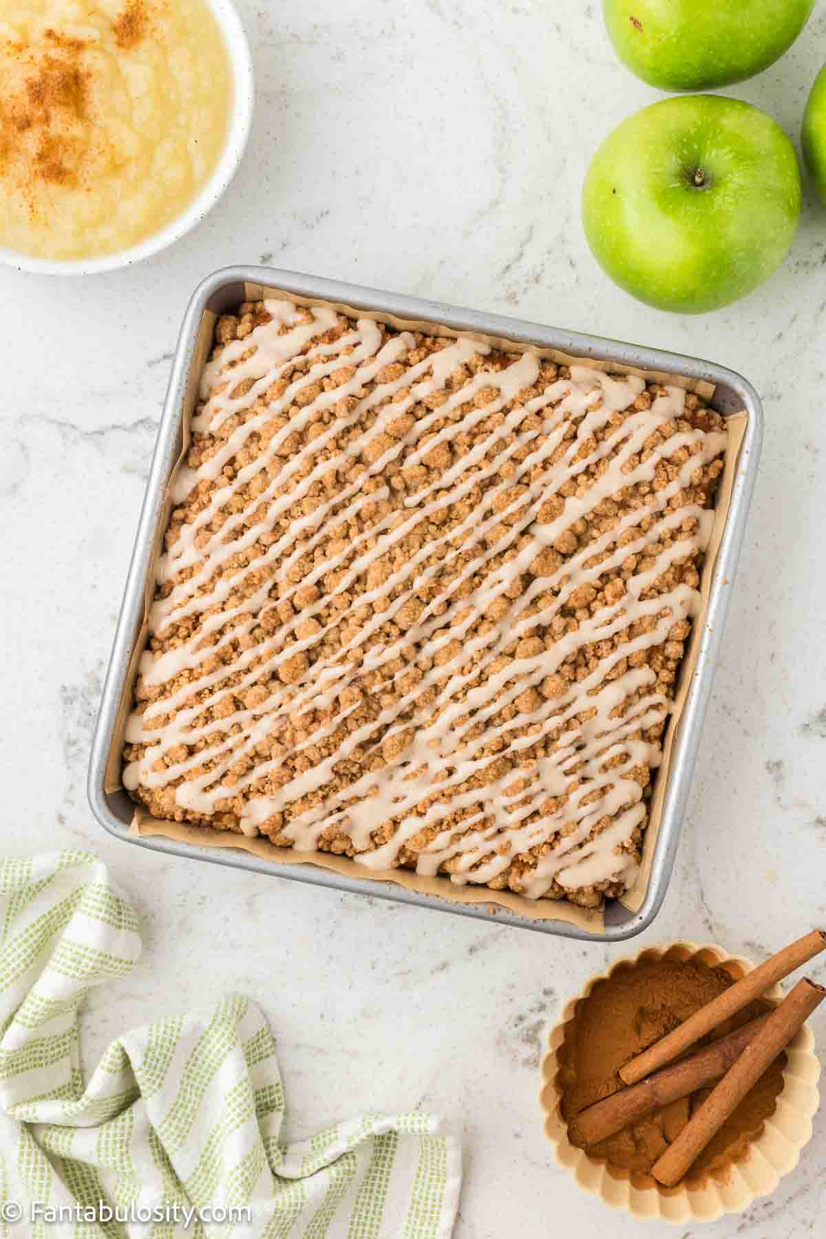Baked, applesauce crumb cake with glaze drizzled on top.