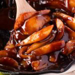 Wooden spoon holding a serving of fried pears, in a cast iron skillet.