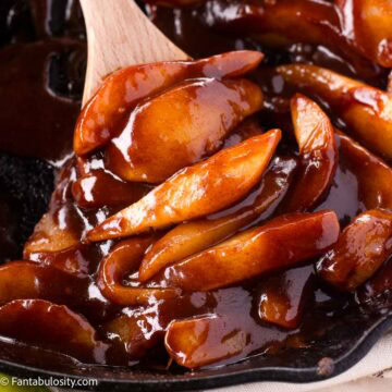 Wooden spoon holding a serving of fried pears, in a cast iron skillet.