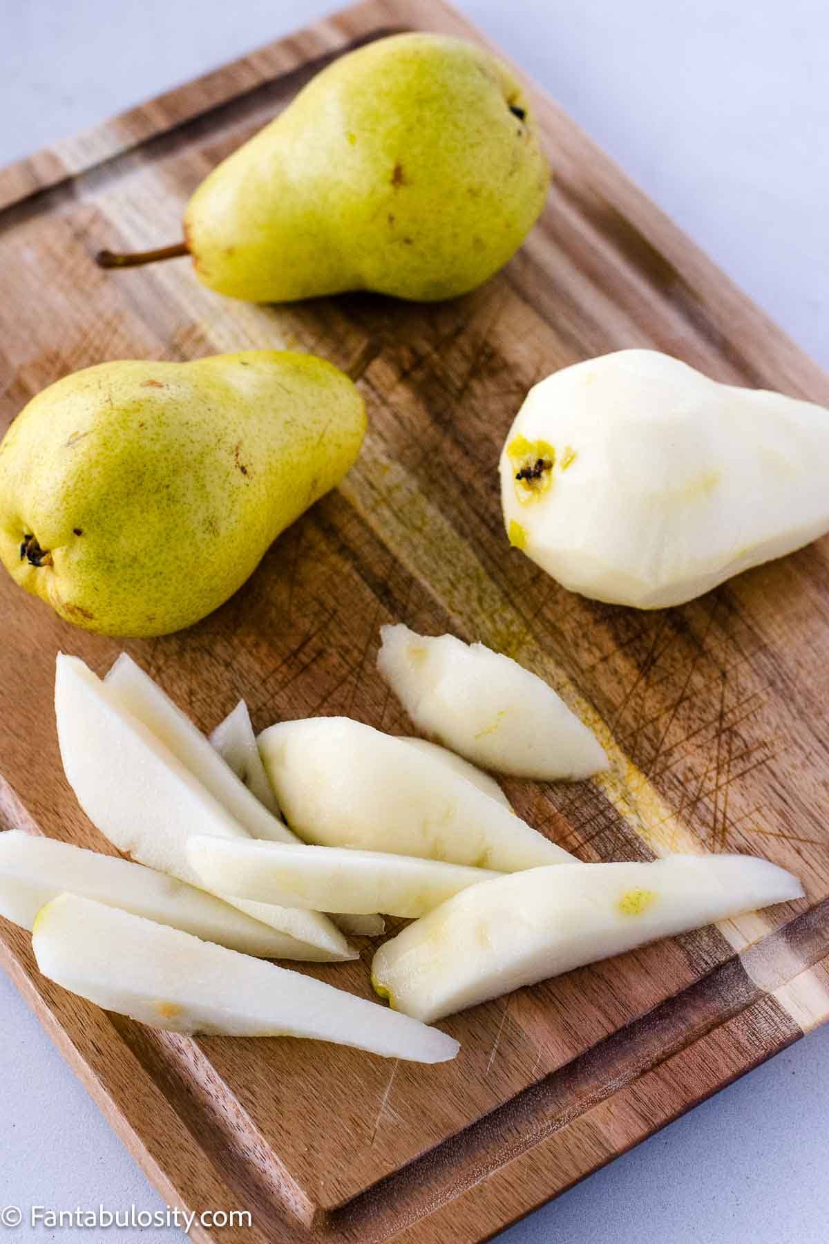 Sliced and peeled pears on wooden cutting board.