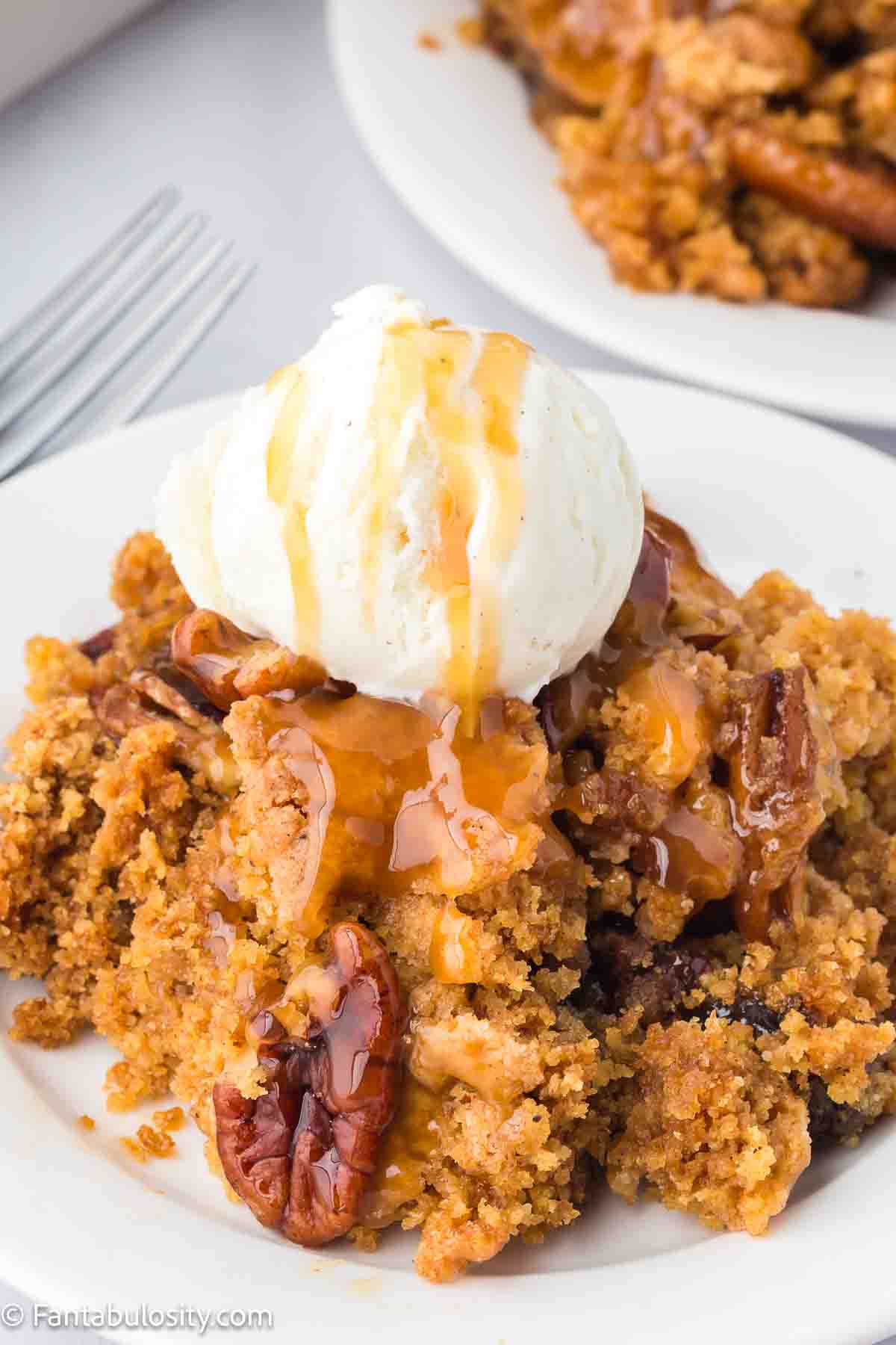 A serving of pecan pie dump cake on a plate, topped with vanilla ice cream.