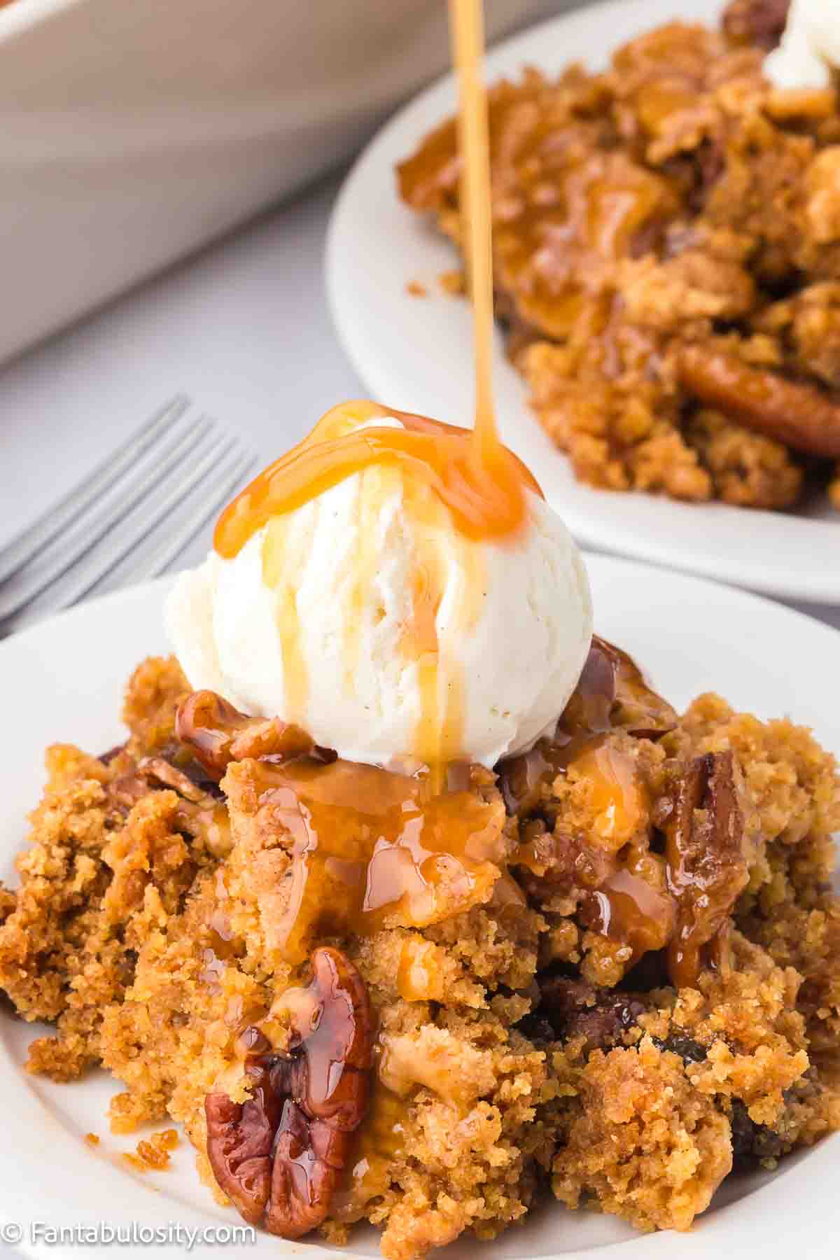 Serving of pecan pie dump cake on a plate, topped with vanilla ice cream and caramel drizzle on top.