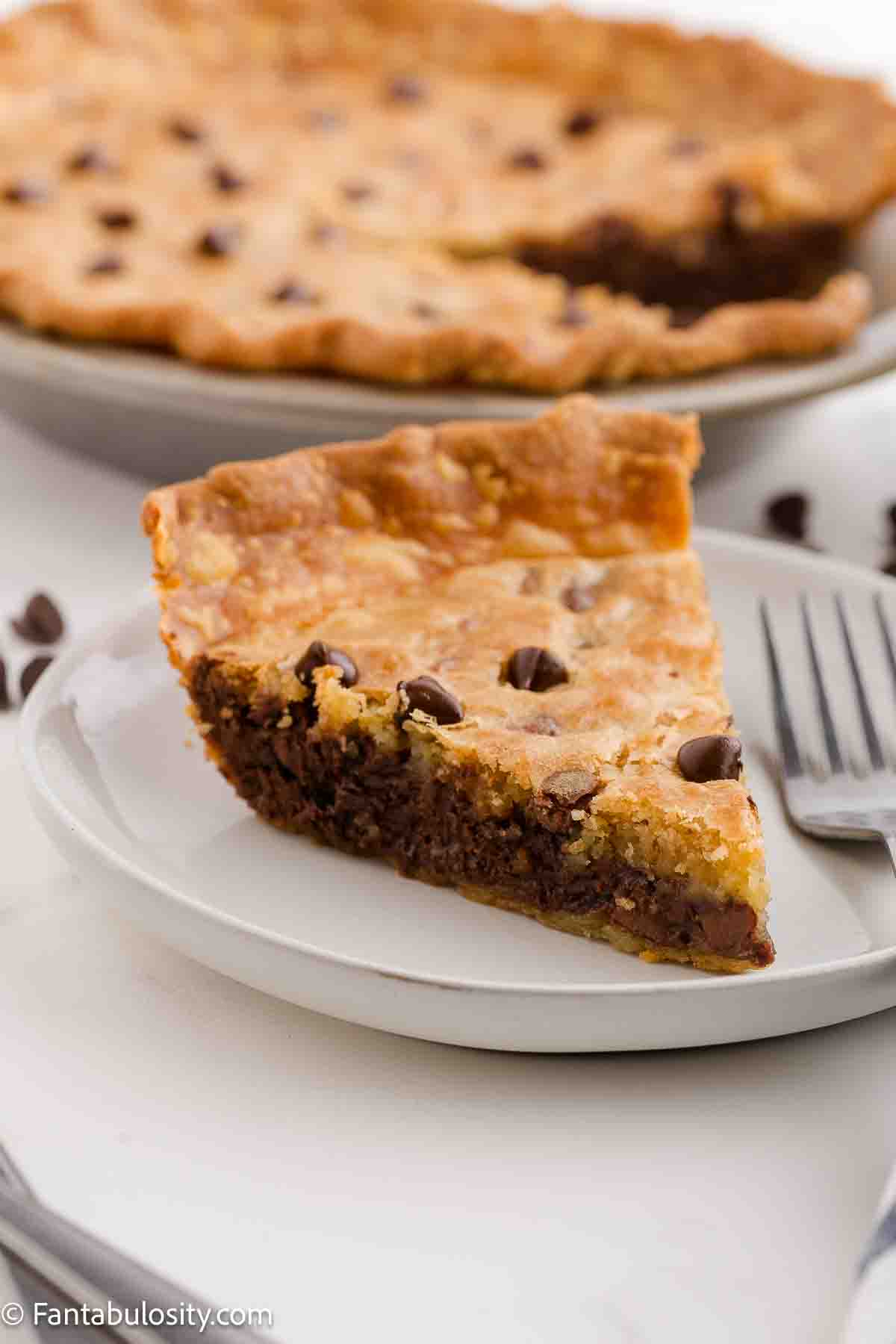 A slice of chocolate chip cookie pie sitting on a plate with a fork.