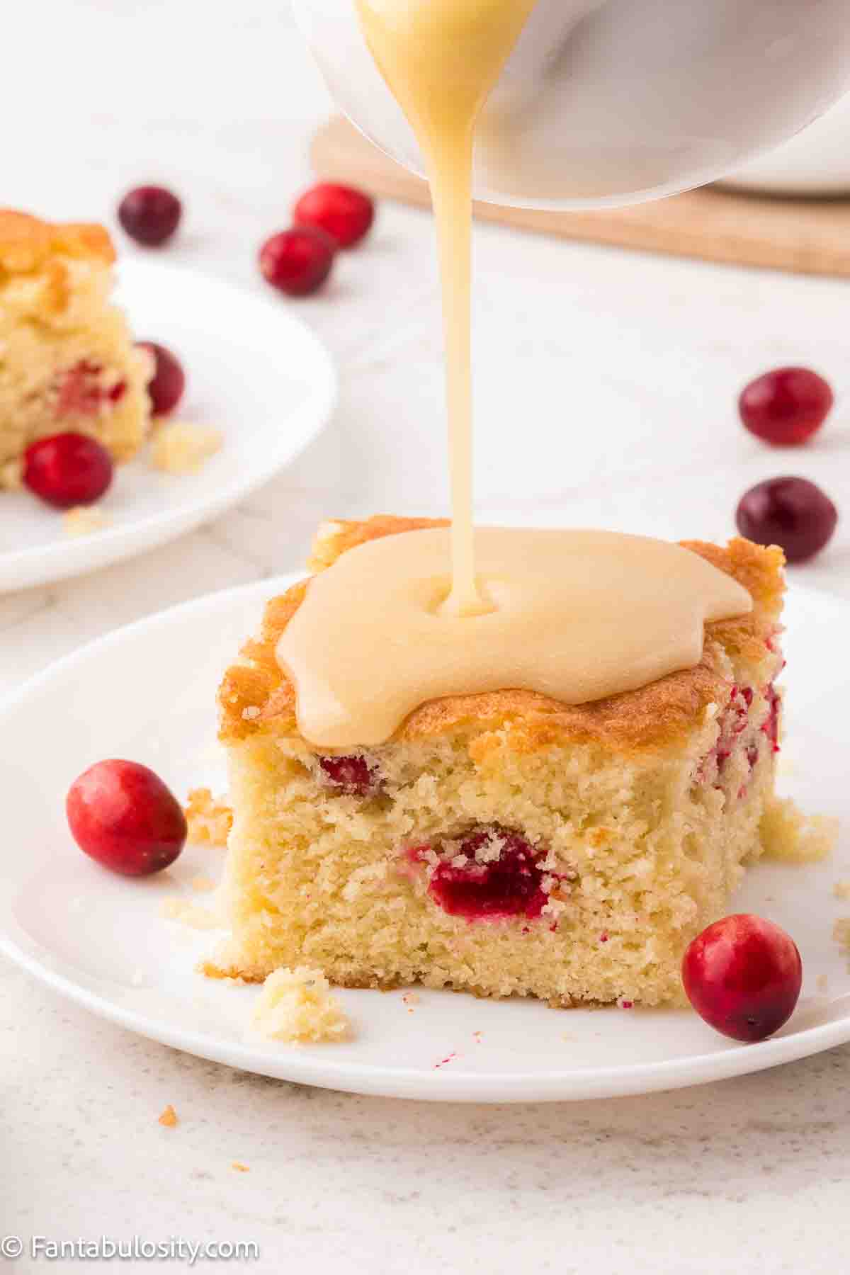 A slice of cranberry cake on plate with butter sauce pouring on the top.