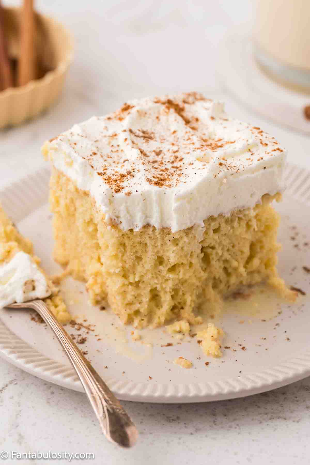 A slice of eggnog tres leches cake on a round plate, next to a fork.