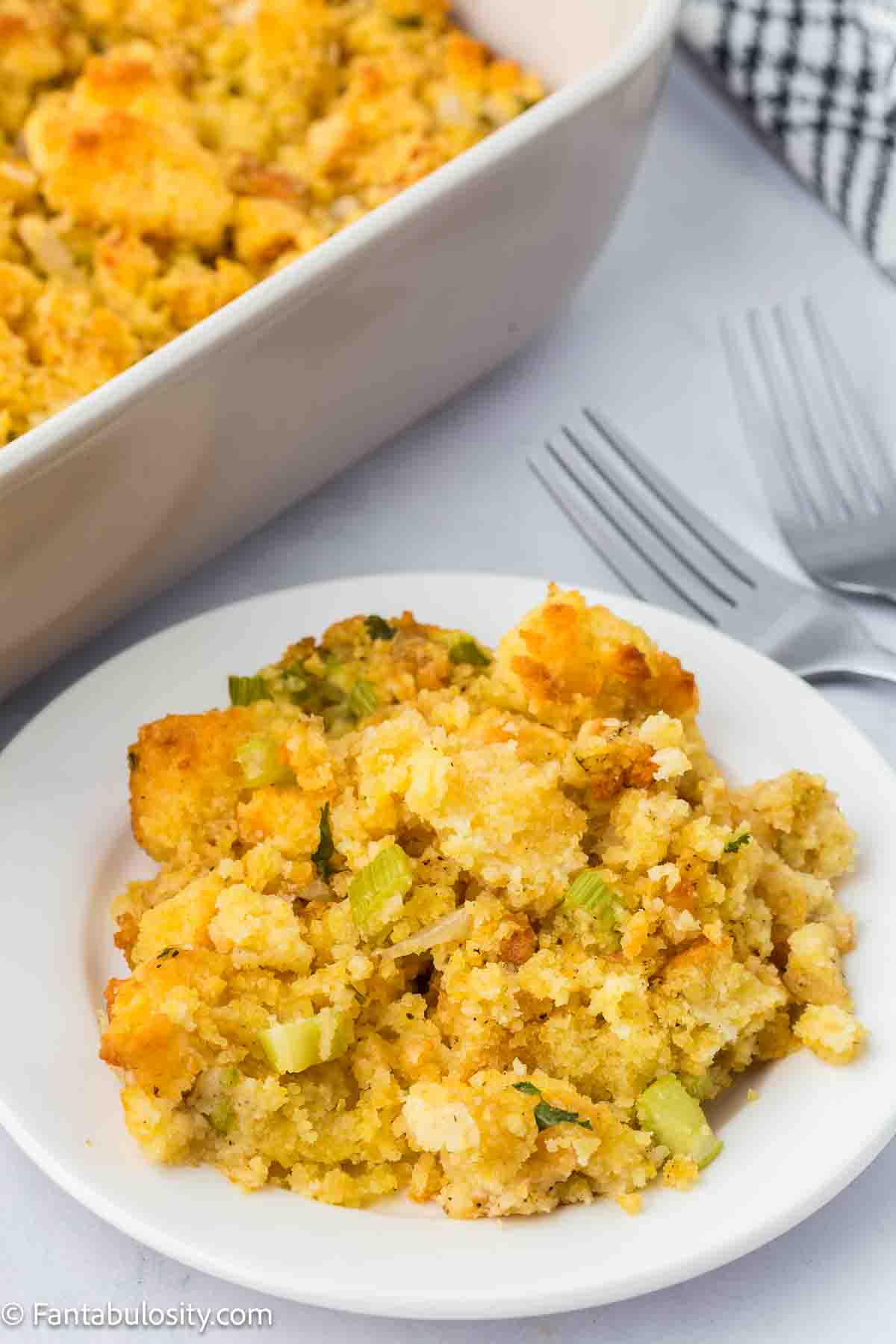 A serving of cornbread dressing on a round plate, next to 9x13 baking dish.