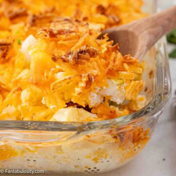 9x13 baking dish with party potatoes inside, and a wooden serving spoon, spooning it out.