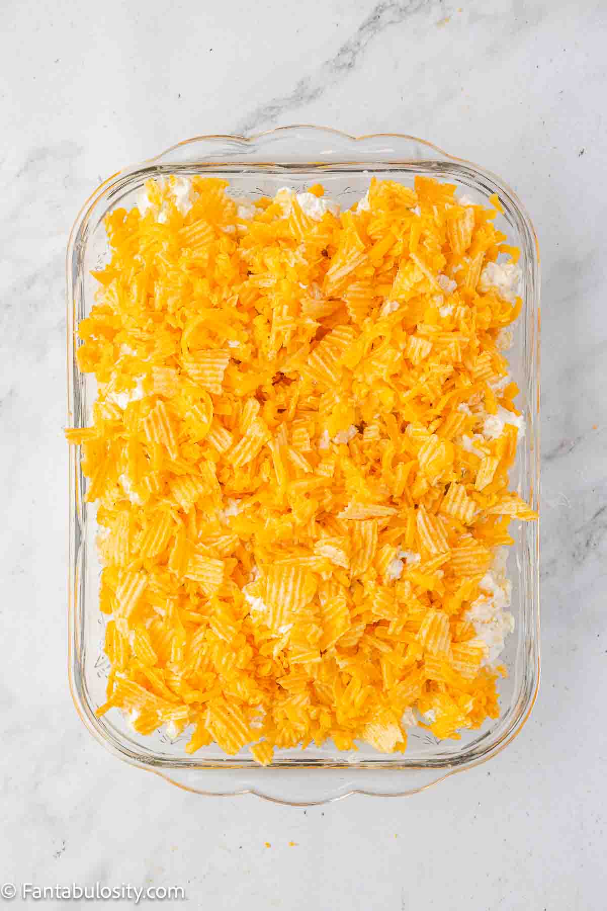 Potato casserole with cheddar and sour cream chips topping, unbaked in baking dish.