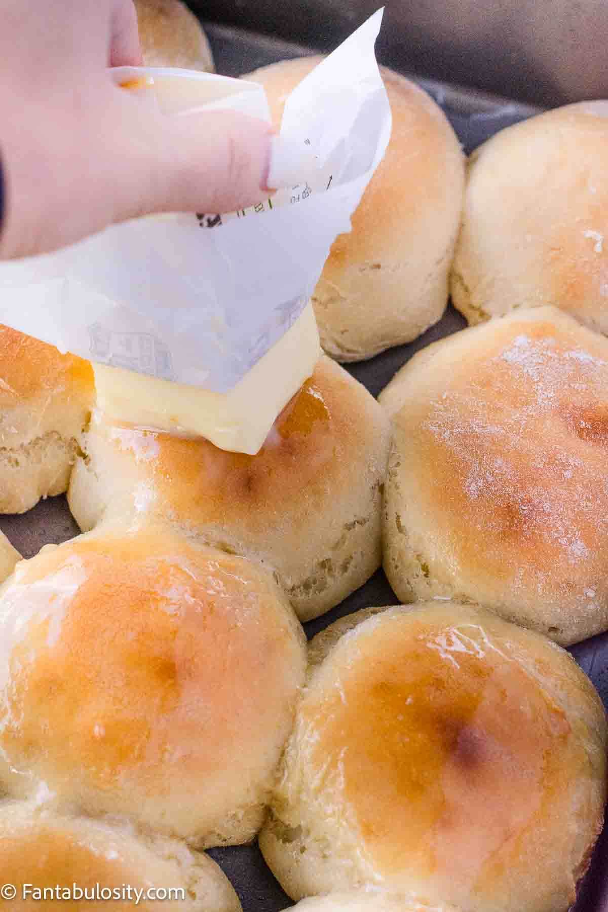 Butter being spread on top of yeast rolls.