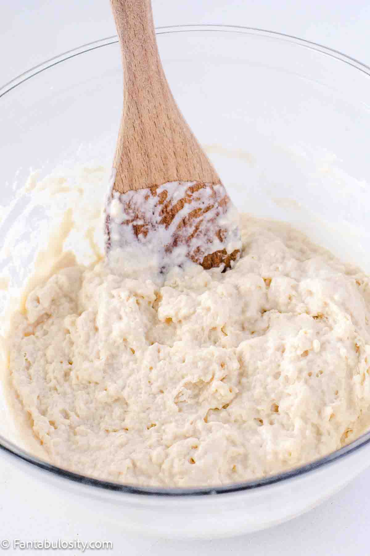 Flour added to yeast mixture and combined to create a roll dough, in mixing bowl.