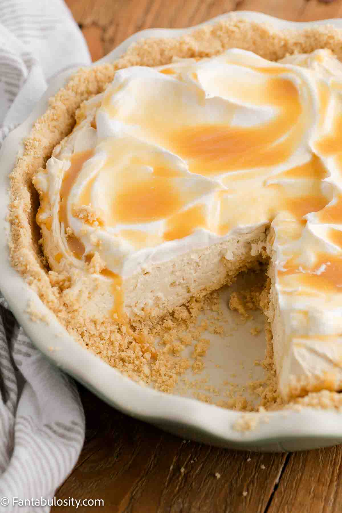 Caramel cream pie with caramel drizzle on top and a piece missing from pie plate.