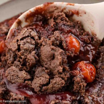 Cherry chocolate dump cake being spooned out of baking dish.