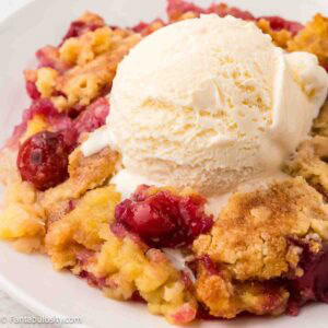 Cherry pineapple dump cake serving on a plate, and topped with a scoop of vanilla ice cream.