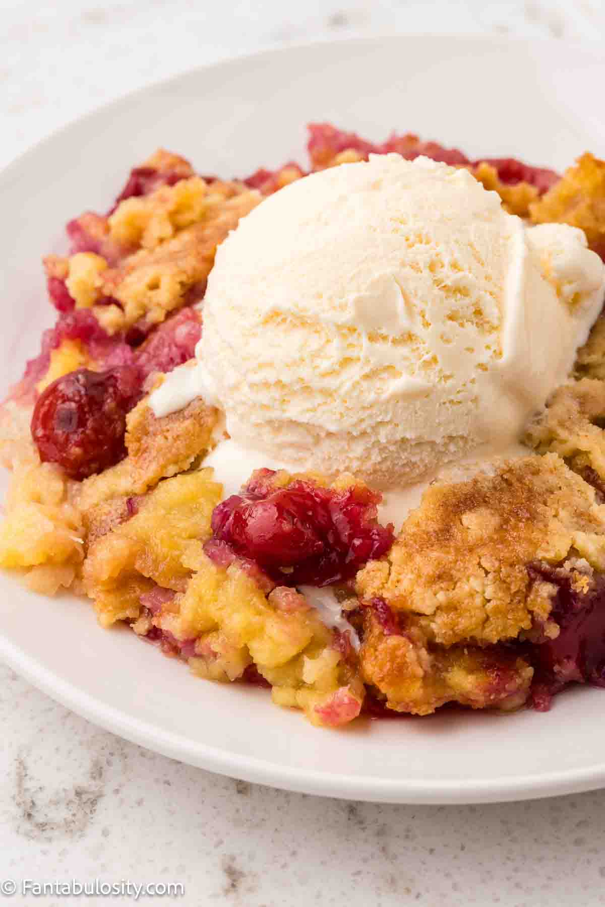 Cherry Pineapple dump cake in a plate, topped with vanilla ice cream.