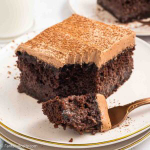 A slice of chocolate Tres Leches cake on a plate, with a fork holding a bite.