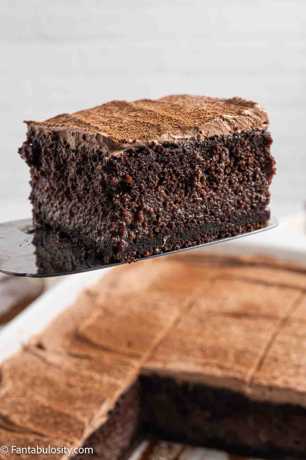 A slice of chocolate tres leches on a spatula above full cake.
