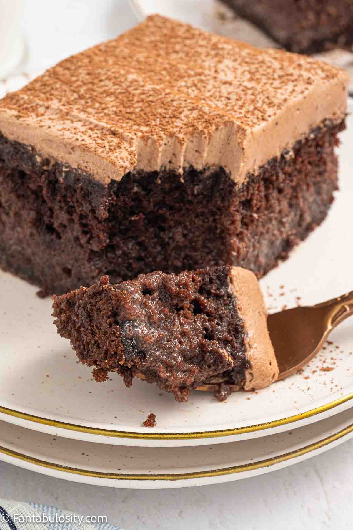 A slice of chocolate tres leches cake on a plate, with a fork that has a bite of cake on it.