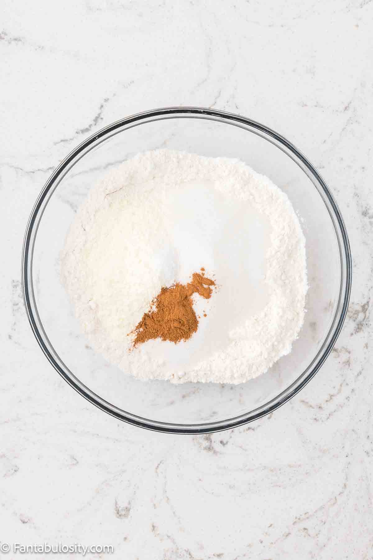 Dry ingredients like cake mix, vanilla pudding mix, and cinnamon in a mixing bowl.