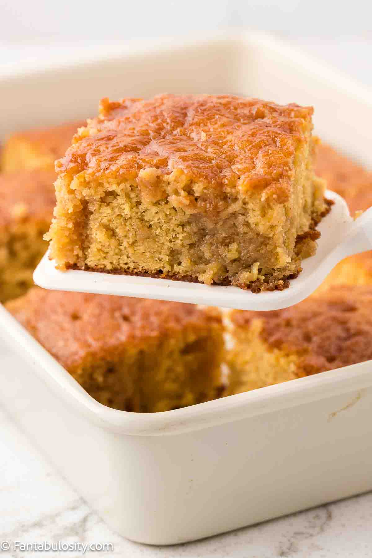 A slice of crack cake on a spatula, being held above rest of cake.