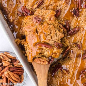 Pecan pie dump cake in 9x13 baking dish, with spoon taking a serving out.