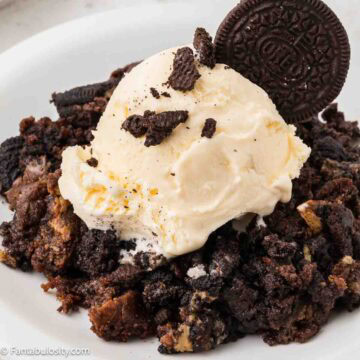 A single serving of Oreo dump cake on a plate, that's topped with a scoop of vanilla ice cream.