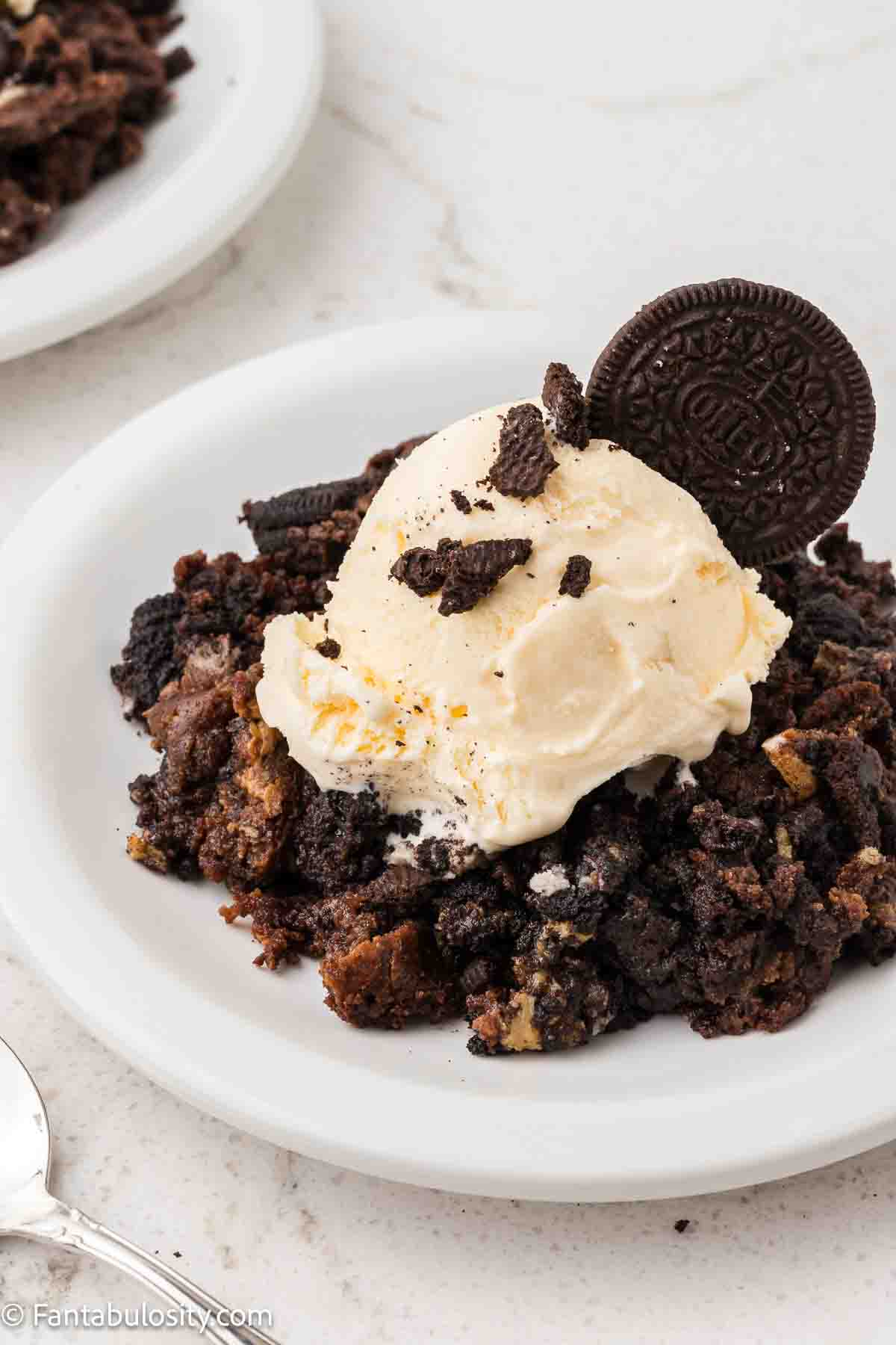 A serving of Oreo dump cake on a round plate, topped with vanilla ice cream.