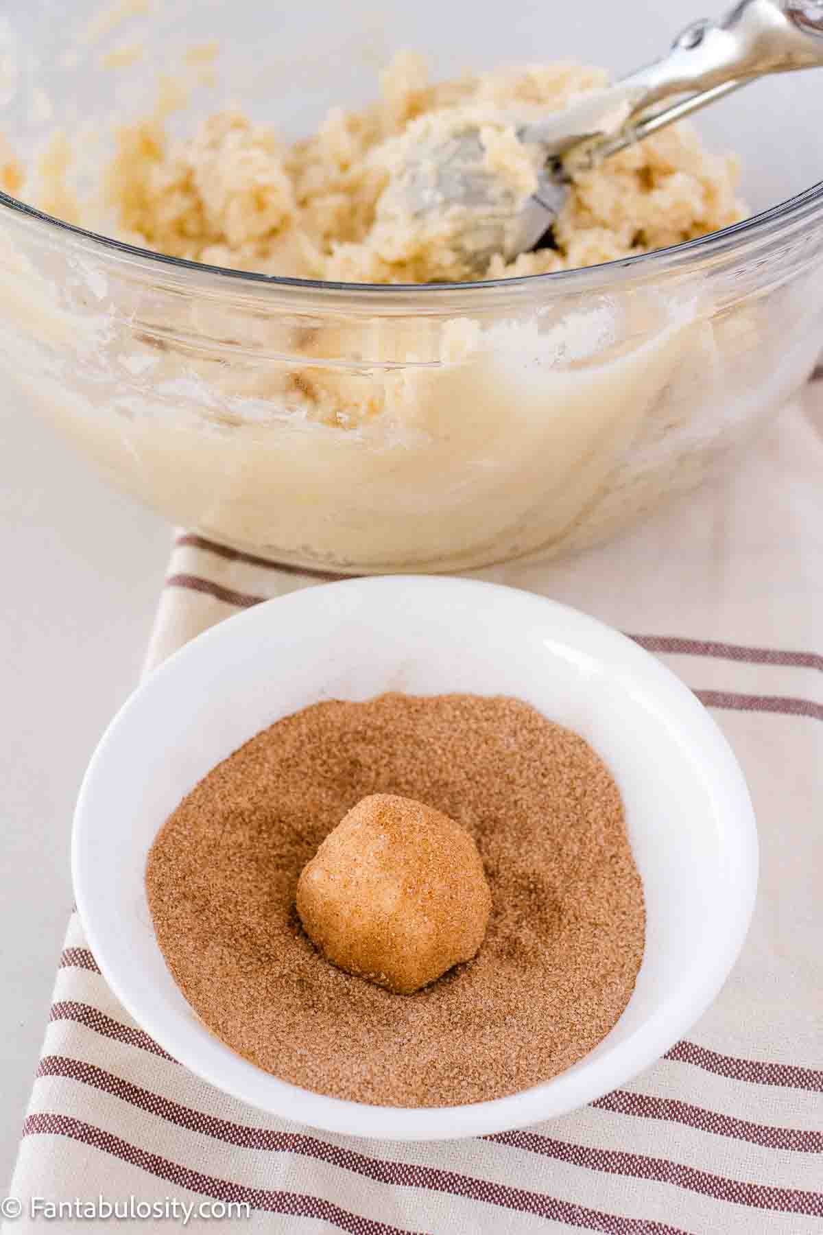 Snickerdoodle cookie dough ball in cinnamon sugar mixture in bowl.
