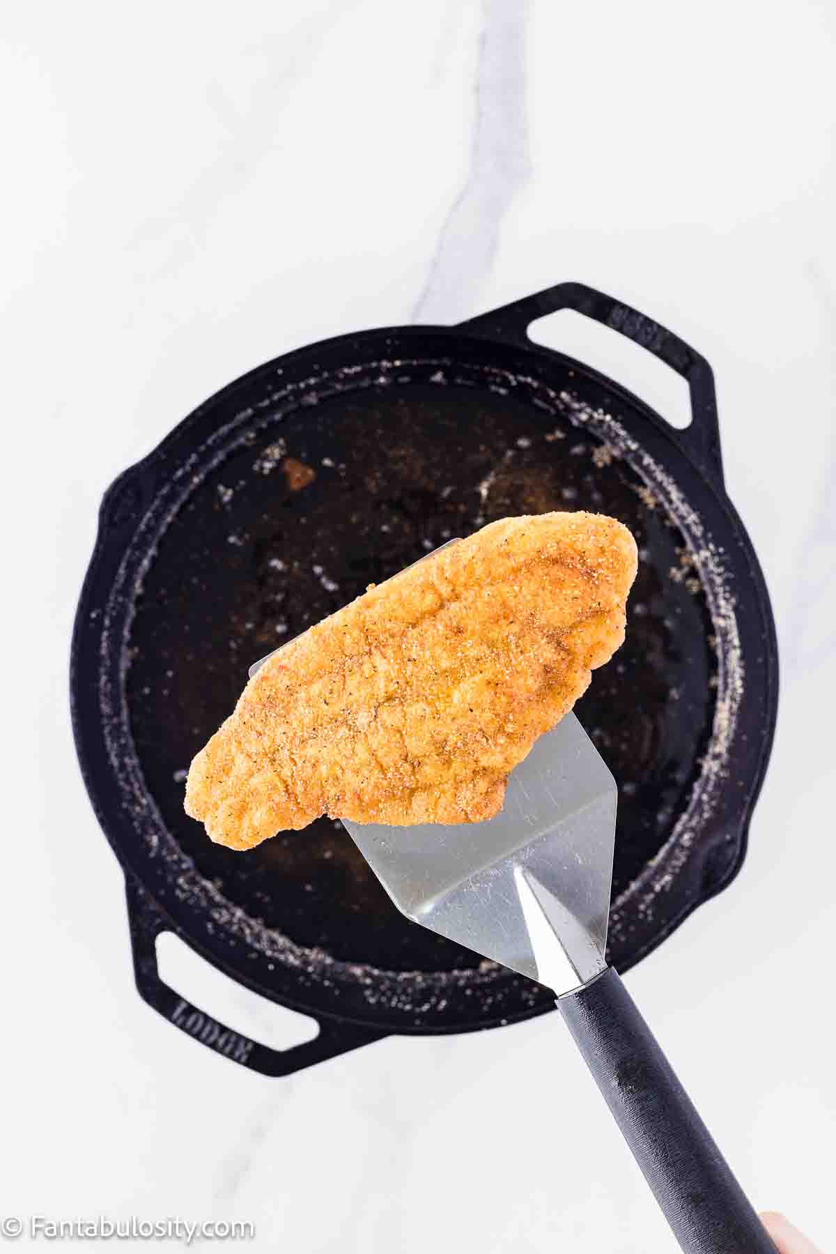 Fried catfish fillet being held over hot oil by a spatula.