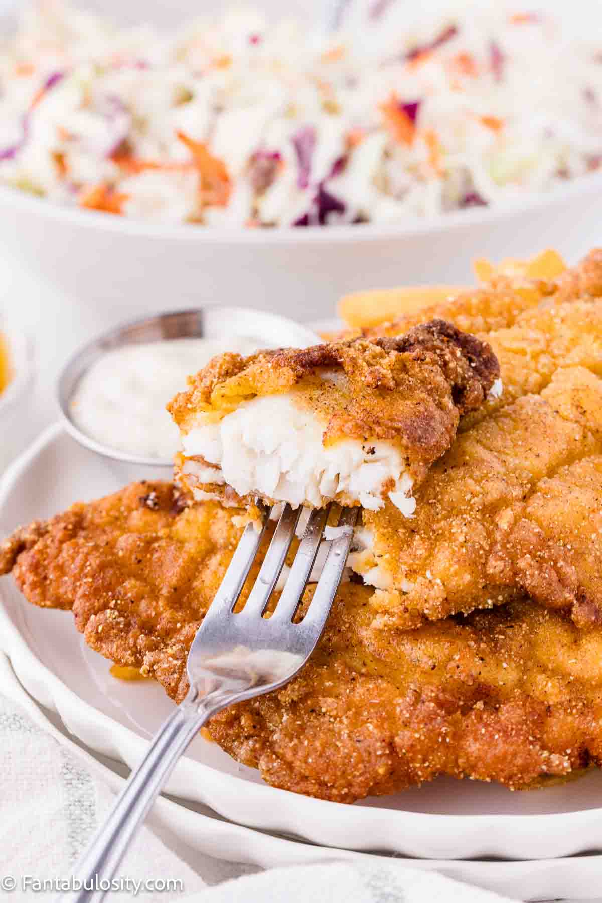 A bite taken off of a fried catfish filet, sitting on top of plate of fried catfish.