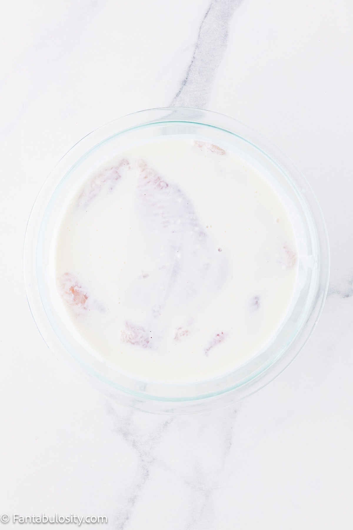 Uncooked catfish soaking in buttermilk and pickle juice mixture.