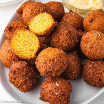 Stack of homemade hush puppies on white plate, with one split open to show the inside.