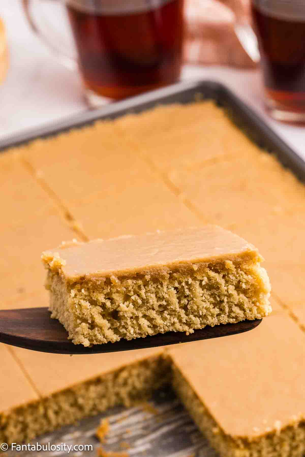 Caramel sheet cake in pan with one slice being held above with spatula. 