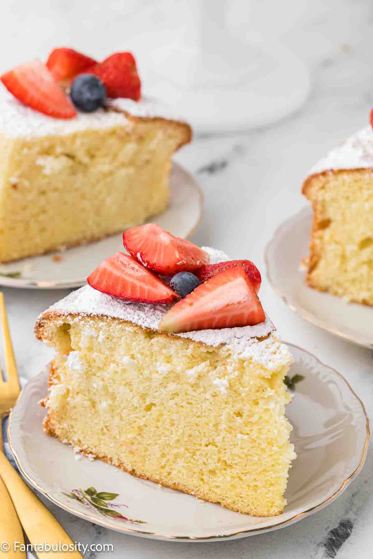 A slice of cloud cake topped with strawberries and blueberries, sitting on round plate.
