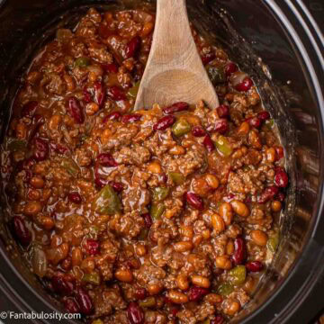 Crockpot baked beans cooked with a wooden spoon resting inside.