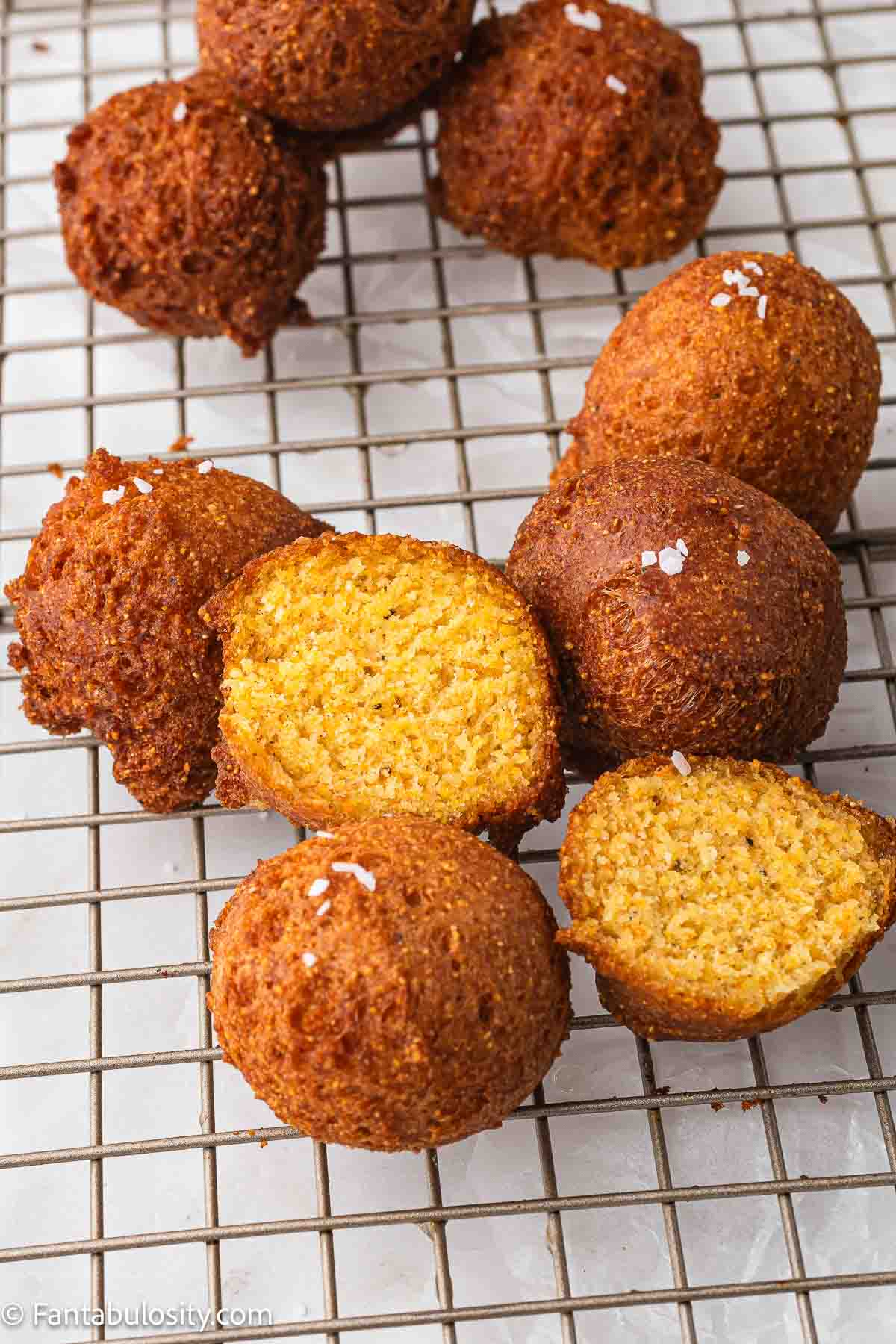 Fried hush puppies on wire rack, with one split open showing the cooked inside.