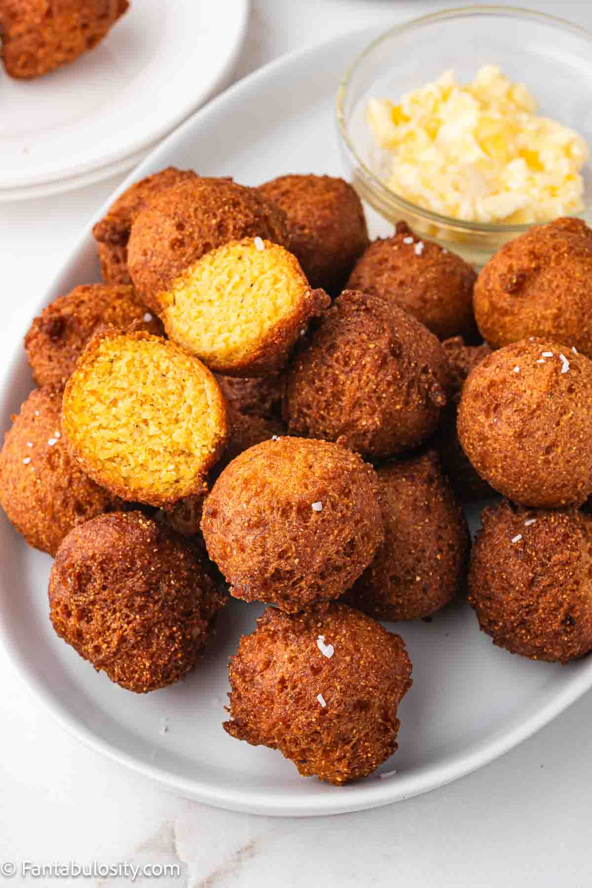 Fried hush puppies on a platter, showing the inside of one hush puppy.