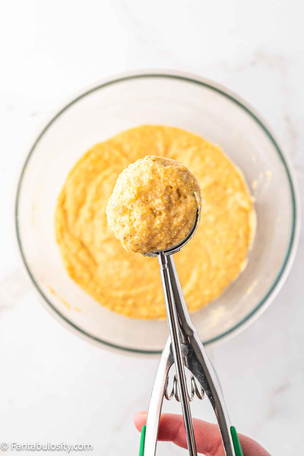 Hush puppy batter being scooped out of mixing bowl, ready for frying in oil. 