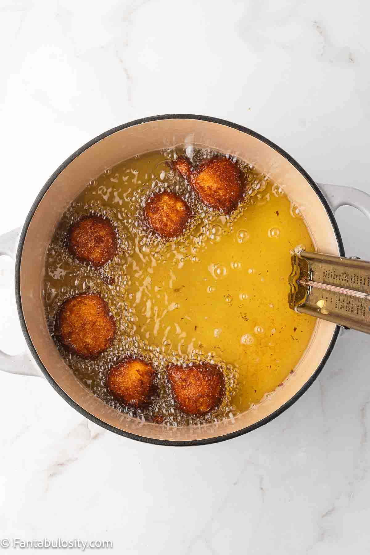 Hush puppies being fried in oil, in pot. 