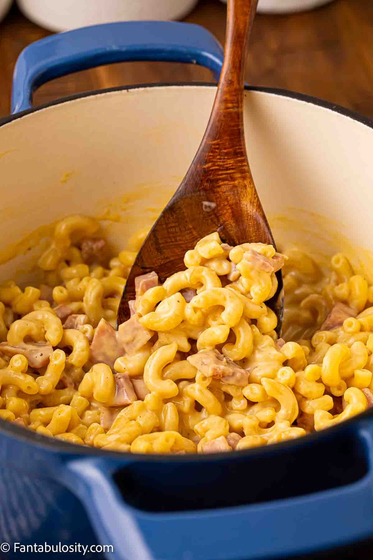 Mac and cheese with ham in dutch oven and a wooden spoon.