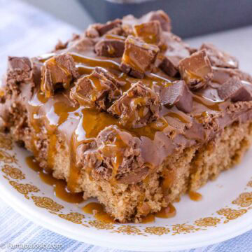 A slice of Milky Way Cake, sitting on a vintage plate, topped with caramel and Milky Way candy bars.
