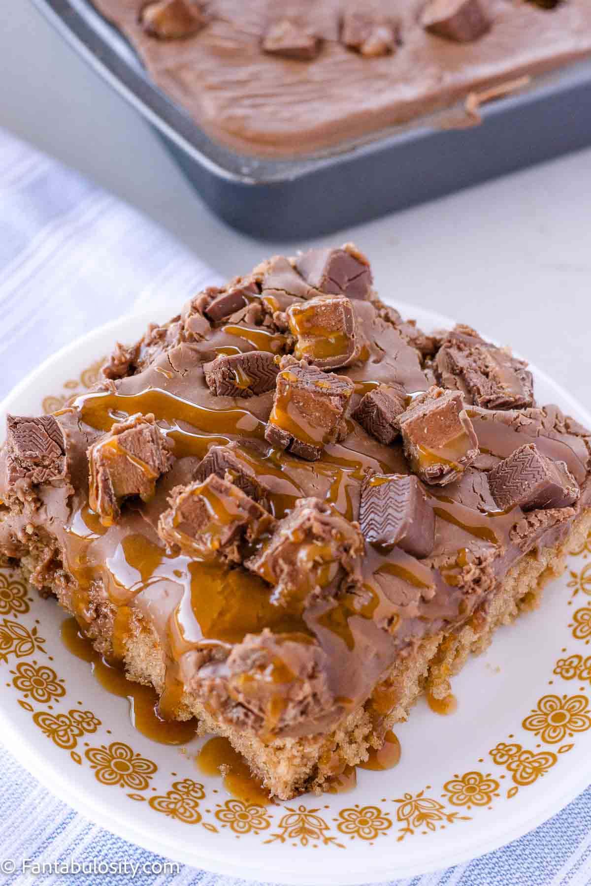 A slice of Milky Way cake on a round plate, topped with Milky Way candy bars.