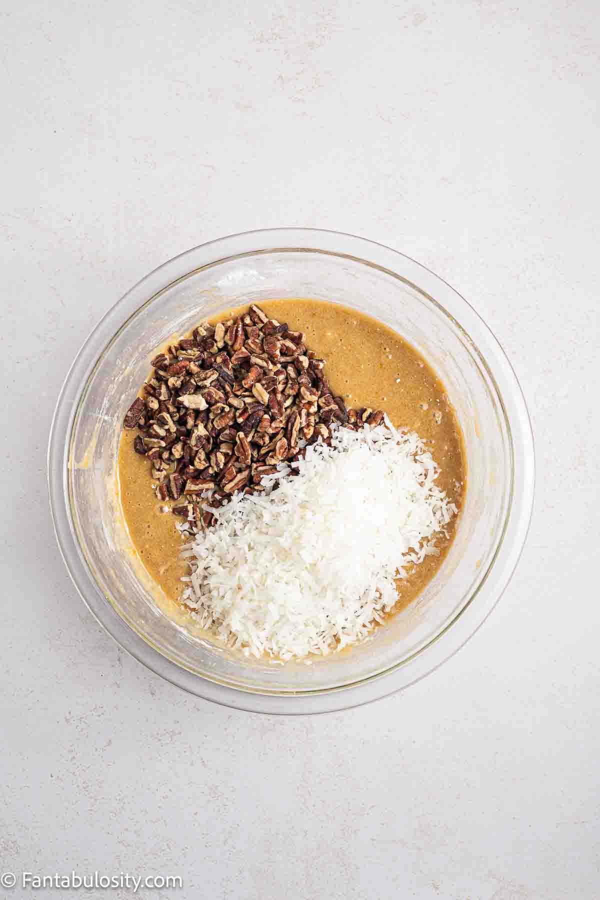Pecans and coconut added to sad cake ingredients mixture in mixing bowl.