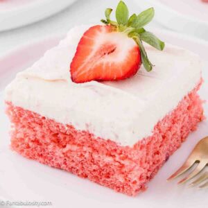 A slice of strawberry jello cake, topped with a strawberry slice, sitting on a round plate.